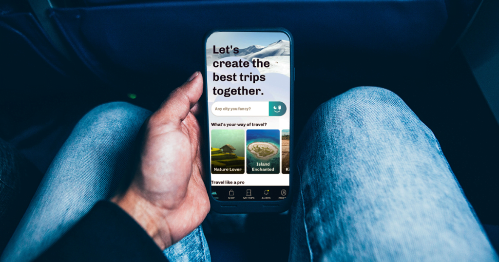 Gambar menunjukkan seorang individu memegang telefon pintar yang memaparkan satu aplikasi pelancongan.